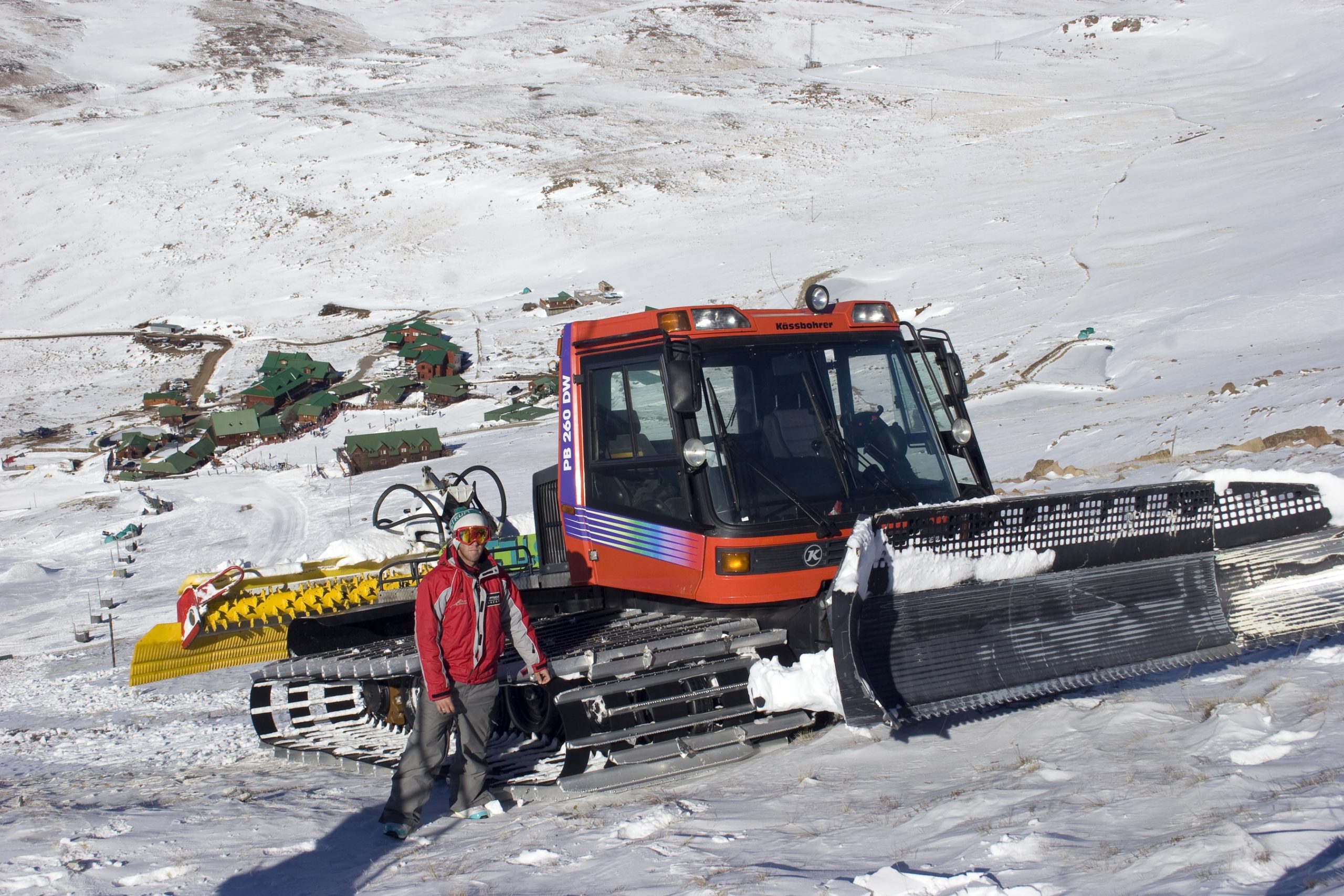 A man stands next to his slope groomer at the top of the slope at Tiffendell, South Africa. Photo from Shutterstock by SAPhotog.