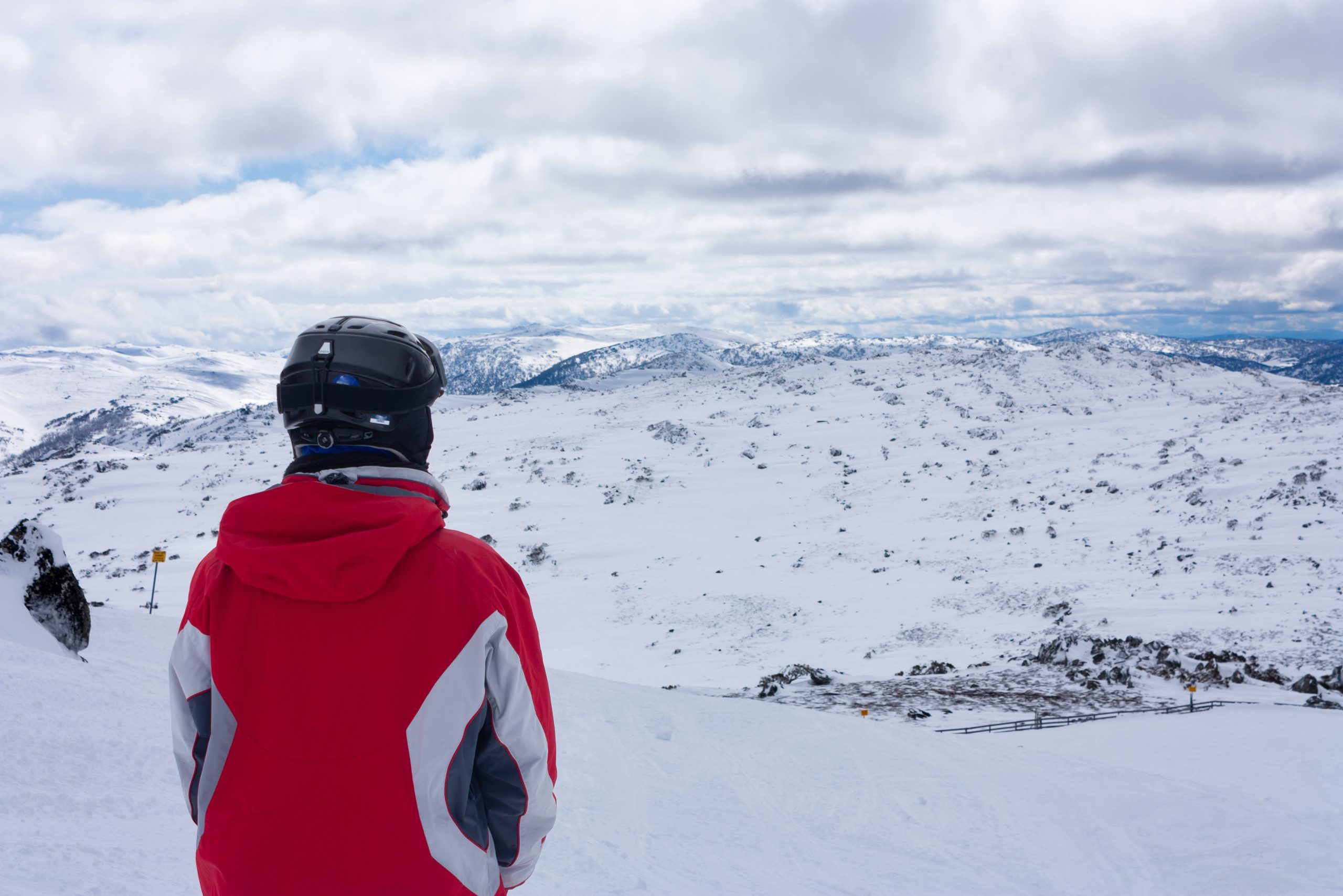 a person in a red coat and helmet looking at a snowy landscape